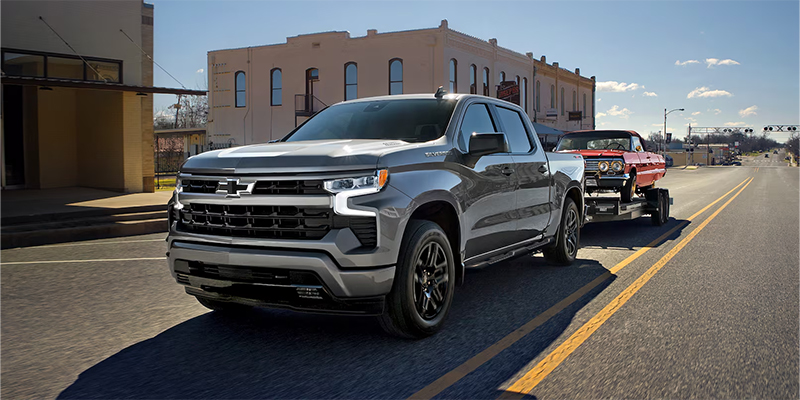 A 2026 Chevrolet Silverado 1500 towing a vintage car behind it.